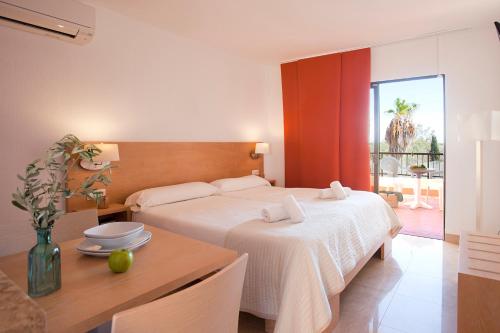 a bedroom with a white bed and a table with a table sidx sidx at Apartamentos Sol Romántica by DOT Suites in Cala Romàntica