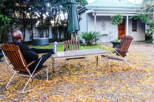 a man sitting at a table in chairs with a laptop at Villa Jana Guesthouse in Pretoria