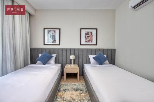 two beds in a room with white walls and blue pillows at Prime Select Galleria New Cairo in New cairo