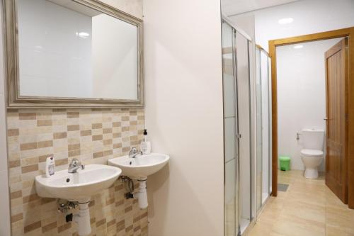 baño con 2 lavabos, espejo y aseo en ALBERGUE EL CAMINANTE, en Portomarín
