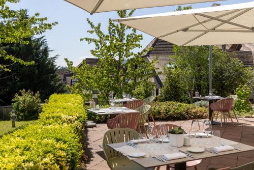 a patio with tables and chairs and an umbrella at Hôtel Val-Vignes Colmar Haut-Koenigsbourg, The Originals Relais in Saint-Hippolyte