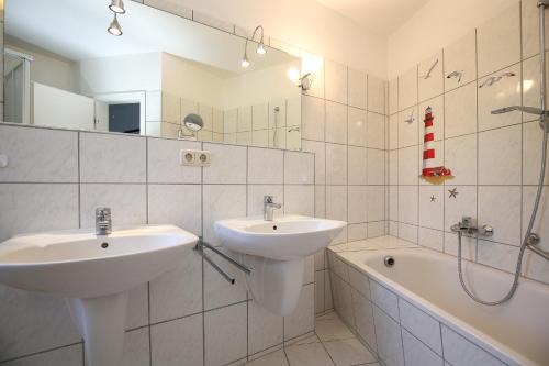a white bathroom with two sinks and a bath tub at Sünnslag Wohnung 122 in Boltenhagen