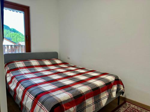 a bed with a plaid blanket in a room with a window at D'Hérens apartment in Breuil-Cervinia