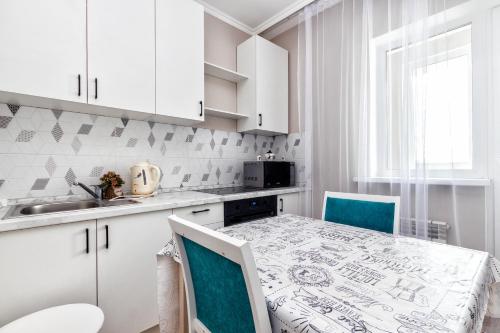 a kitchen with white cabinets and a table and chairs at ЖК Арман Кала in Prigorodnyy