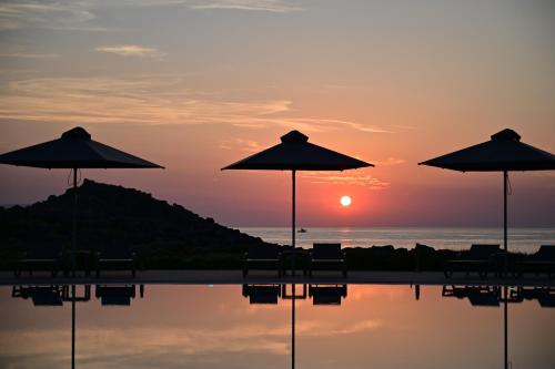 a pool with chairs and umbrellas in front of a sunset at Kavos Hotel & Suites in Stavros