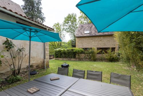 a table and chairs with a blue umbrella in a yard at Domaine Les Maurelles in Milhac