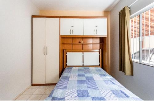 Cette chambre comprend un lit, des armoires blanches et une fenêtre. dans l'établissement Casa aconchegante à 200m da praia, à Rio das Ostras