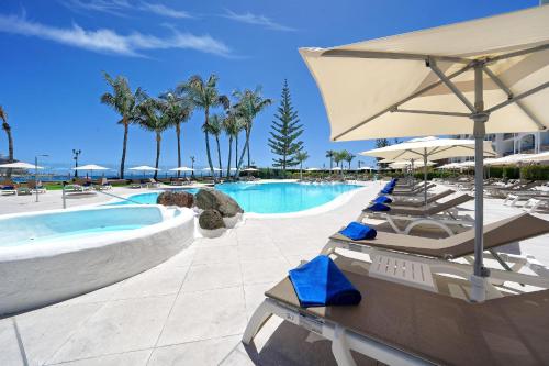a pool with chairs and umbrellas in a resort at H10 Costa Mogán - Adults Only in Playa del Cura