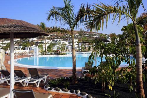 una piscina en un complejo con palmeras y sillas en Labranda Alyssa Suite Hotel, en Playa Blanca