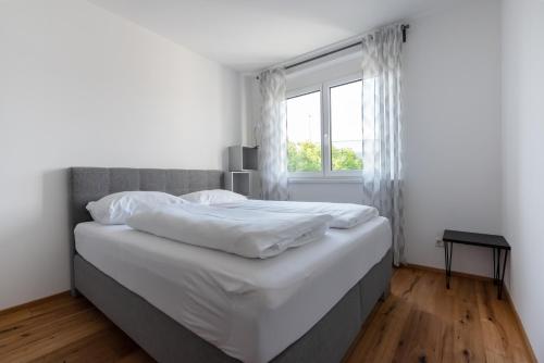 a white bedroom with a large bed and a window at Grüne Ruhelage, 20 Minuten ins Zentrum und Parkgarage in Vienna