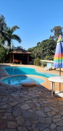 uma piscina com um guarda-sol e uma mesa em Chácara Tâmonamió - Casa de campo completa para sua família - WIFI fibra em Limeira
