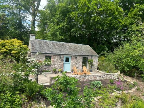 a stone cottage with a blue door and two chairs at Charming stone Bothy at Loch Lomond in Luss