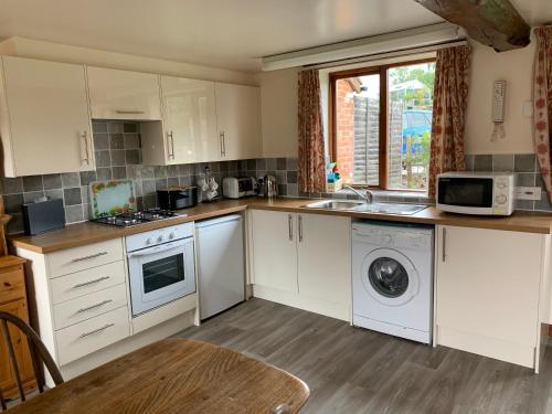 cocina con armarios blancos, lavadora y secadora en Irelands Farm Cottages en Birmingham