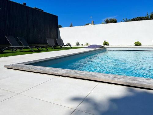 une piscine avec des chaises à côté d'un bâtiment dans l'établissement L'échappée - Villa avec piscine, à La Genilliere