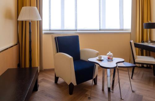 a room with a table and a blue chair and a small table with a cup at UNA Hotels Malpensa in Cerro Maggiore