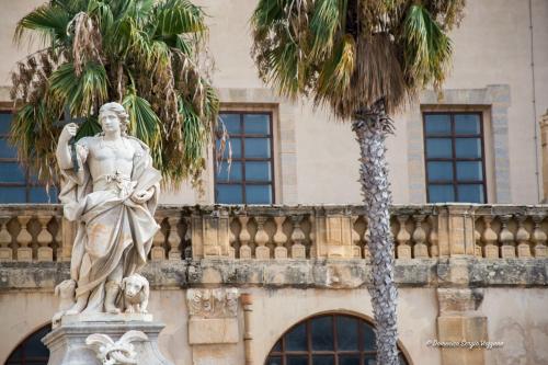 a statue in front of a building with palm trees at Casa Dalfea in Mazara del Vallo