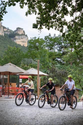 trois personnes faisant du vélo sur une route avec une montagne en arrière-plan dans l'établissement Huttopia Gorges du Tarn, aux Vignes