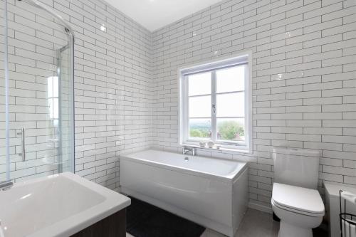 a white bathroom with a tub and a toilet and a window at Stylish 2-bed Duplex Stunning Malvern views Peaceful Getaway in Malvern Wells