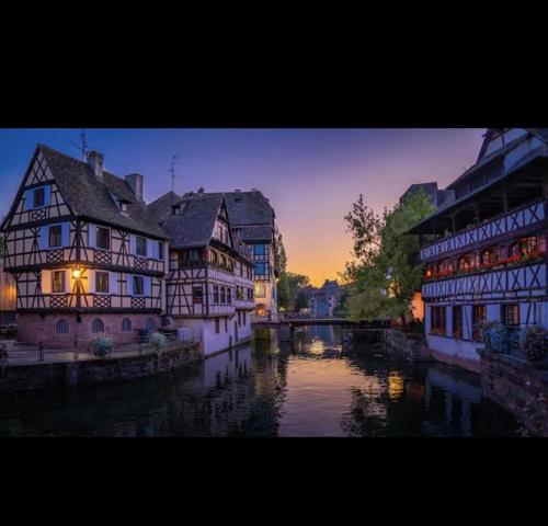 a group of buildings next to a river at sunset at Gite Junior L'Ecrin du Ried PROCHE EUROPA-PARK in Artolsheim