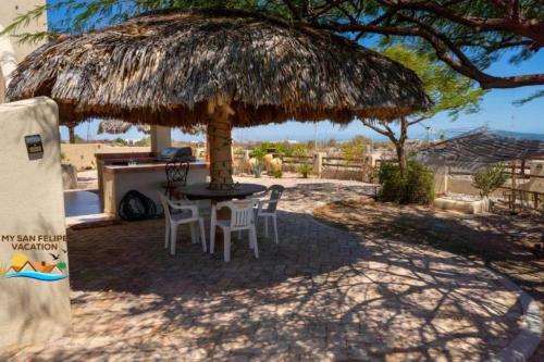 a table and chairs under a straw umbrella at Mountain side Delight - Palapas house San Felipe Vacation Rental in Playa El Paraíso