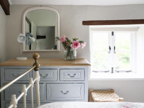 a bedroom with a mirror and a vase of flowers at Friesland Cottage in Shilton