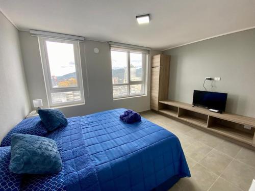 a bedroom with a blue bed and two windows at Epicentro, departamento estudio, sin balcón, con estacionamiento in Temuco