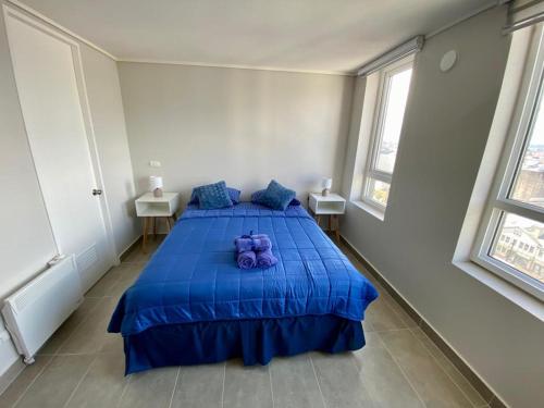 a bedroom with a blue bed with two windows at Epicentro, departamento estudio, sin balcón, con estacionamiento in Temuco