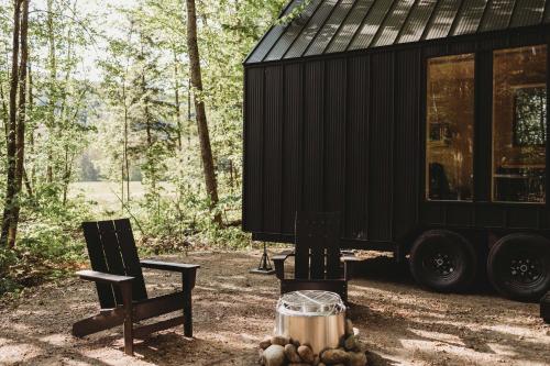 a black tiny house sitting next to two chairs at Lumen Nature Retreat in Woodstock
