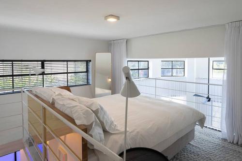 a white bedroom with a bed and some windows at A Bauhaus Gem - Prime Location in Tel Aviv