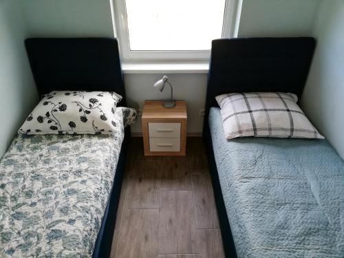 two beds in a room with a night stand and a window at Lazurowy Zakątek in Dąbki