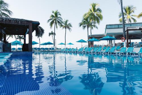 una piscina con sillas, sombrillas y palmeras en Fontan Ixtapa, en Ixtapa