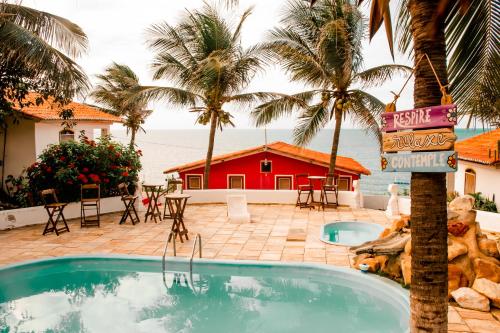 a swimming pool with palm trees and a red house at Lua Morena in Aracati