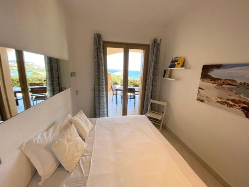 1 dormitorio con cama blanca y vistas al océano en A Punta Tegge il mare la spiaggia il tramonto, en La Maddalena