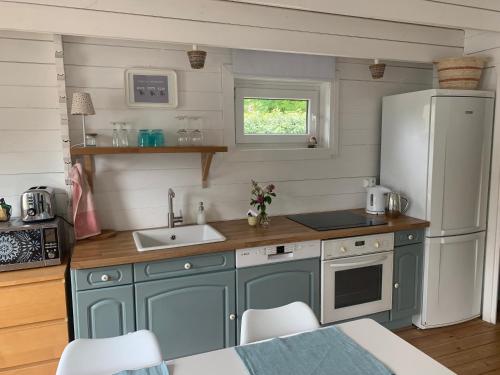 La cuisine est équipée de placards bleus et d'un réfrigérateur blanc. dans l'établissement Cottage Le Cerf-volant, à Saint-Aubin-sur-Mer