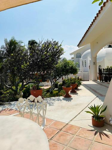 a patio with white chairs and trees and a house at Villas Fasol Huatulco in Santa Cruz Huatulco