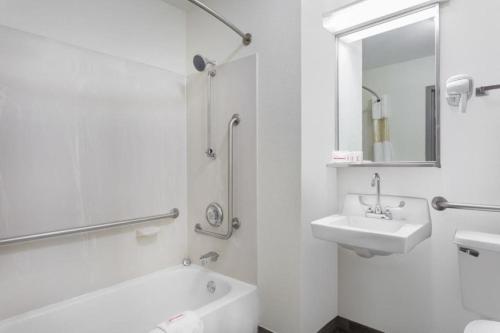 a white bathroom with a sink and a tub and a mirror at Clarion Pointe - Greensboro Coliseum Area in Greensboro