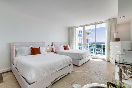 a white bedroom with two beds and a balcony at Ocean View Balcony steps from Restaurants, Peacock Park & Marina in Miami