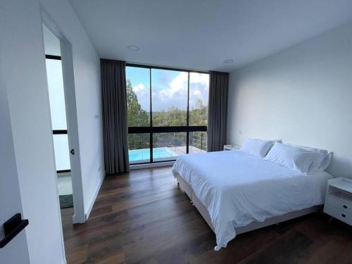 1 dormitorio con cama blanca y ventana grande en Aqua Guatapé - Lakeside Luxury Villa, en Guatapé