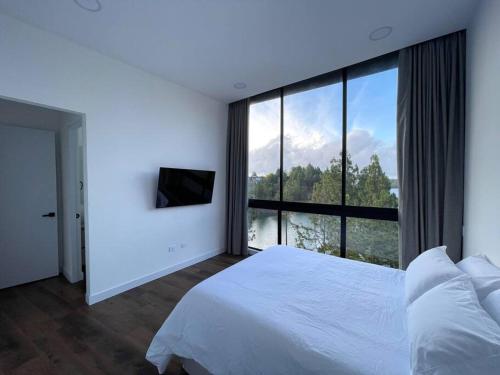 1 dormitorio con cama blanca y ventana grande en Aqua Guatapé - Lakeside Luxury Villa, en Guatapé