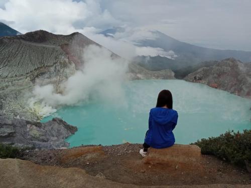 a woman sitting on the edge of a cliff looking at a blue lake at Ijen Farmer Homestay in Banyuwangi