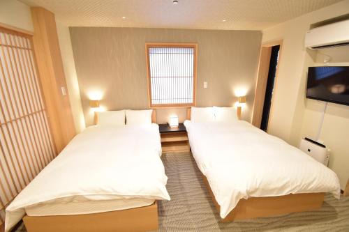 two beds in a hotel room with a tv at K-style 東本願寺 in Kyoto