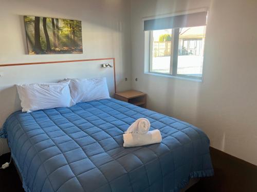 a bedroom with a blue bed with a towel on it at Pinewood Motels in Fairlie