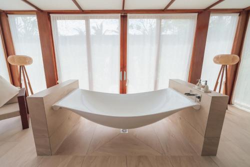 a white bath tub in a room with windows at Fusion Resort Cam Ranh - All Spa Inclusive in Cam Ranh
