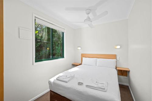 a bedroom with a bed with white sheets and a window at Sapphire Beach Holiday Park in Coffs Harbour