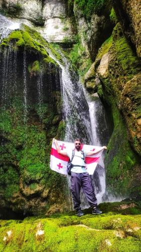 a man is standing in front of a waterfall at Guest House Balda in Martvili