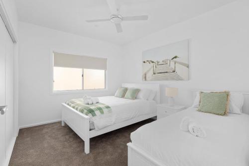 a white bedroom with two beds and a window at HideAwayII at Shoal Bay in Shoal Bay