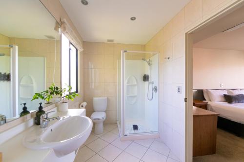 a bathroom with a sink and a shower and a bed at Harvest Lodge Motel in Havelock North