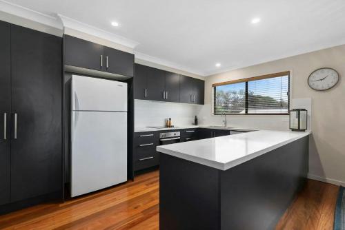 a kitchen with black cabinets and a white refrigerator at Sun Dance Peregian Beach in Peregian Beach