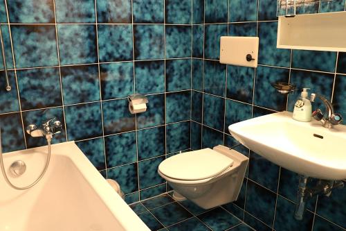 W wyłożonej niebieskimi kafelkami łazience znajduje się toaleta i umywalka. w obiekcie Chesa Dominium w mieście Bergün