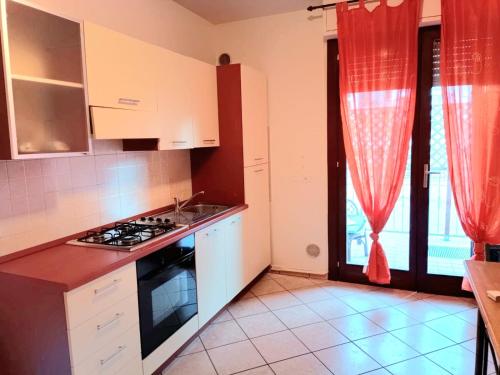 a kitchen with a stove and a window with red curtains at Alba Sweet in Alba Adriatica